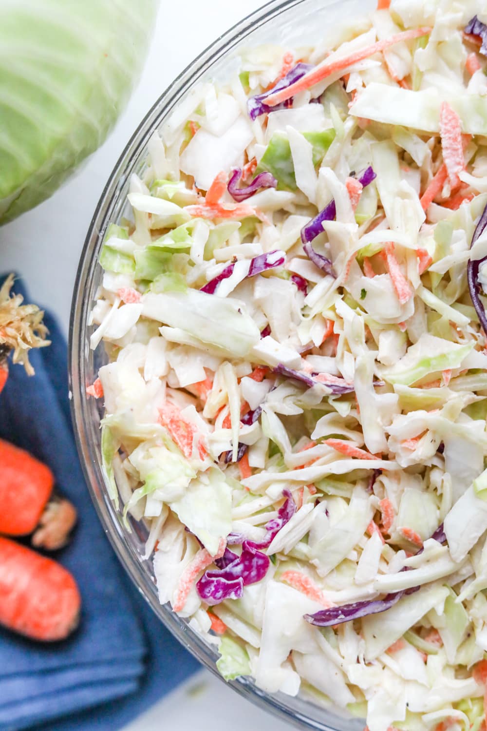 Low carb coleslaw in a bowl next to carrots and green cabbage.