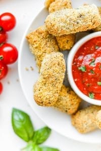 Low carb mozzarella sticks next to a cup of marinara sauce.