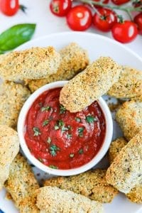 Keto cheese sticks on a plate next to a cup of low carb marinara sauce.