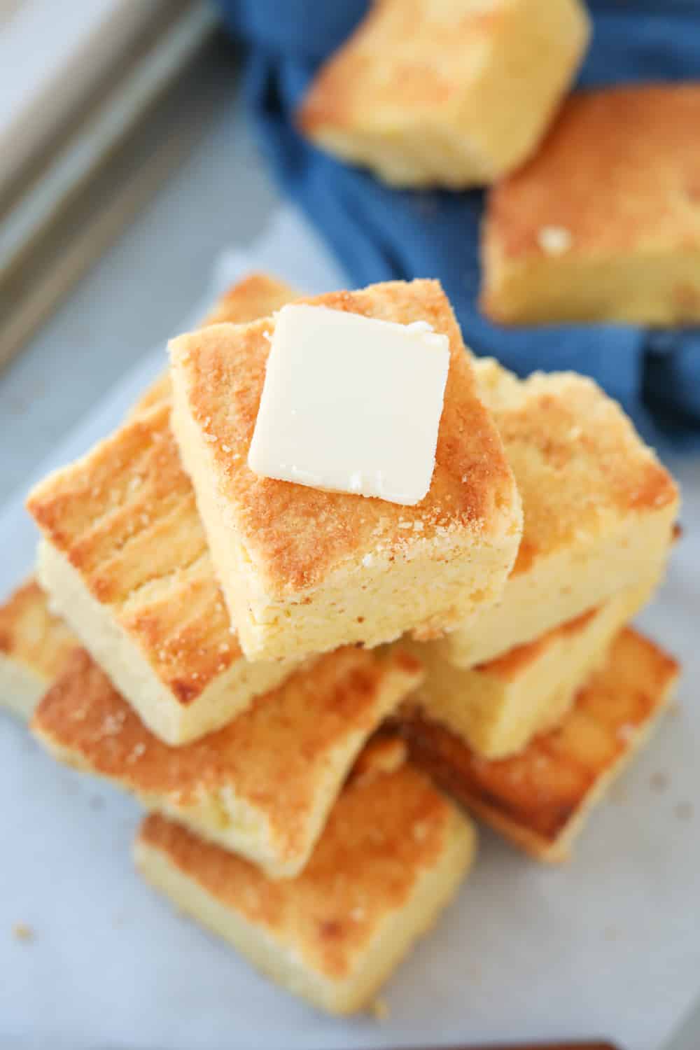Cornbread slices stacked on top of one another with the top slice covered in butter