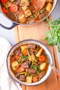 A bowl of keto beef stew next to fresh herbs.