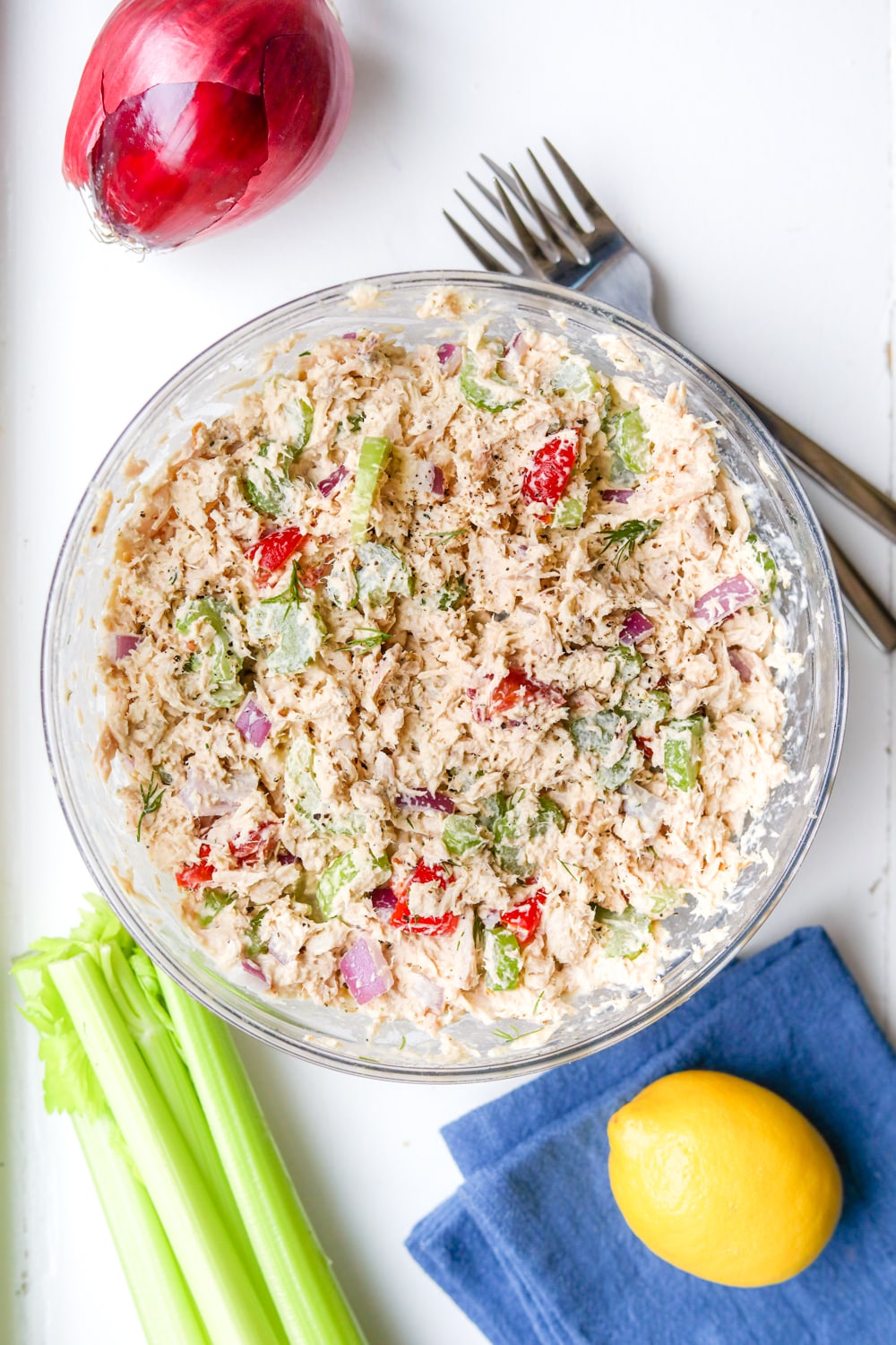 A large bowl of keto tuna salad with vegetables, a lemon, and two forks next to it.