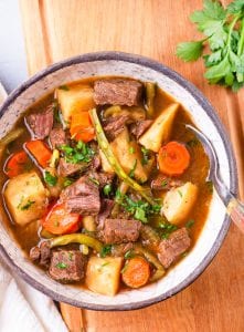 A bowl of beef stew with topped with fresh herbs.