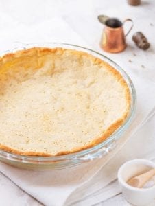 A low carb pie crust that has been cooked in a pie plate, and is set on top of a white towel.