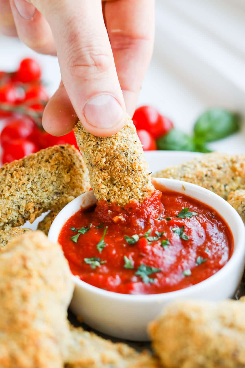 A hand dipping a mozzarella stick into marinara sauce.