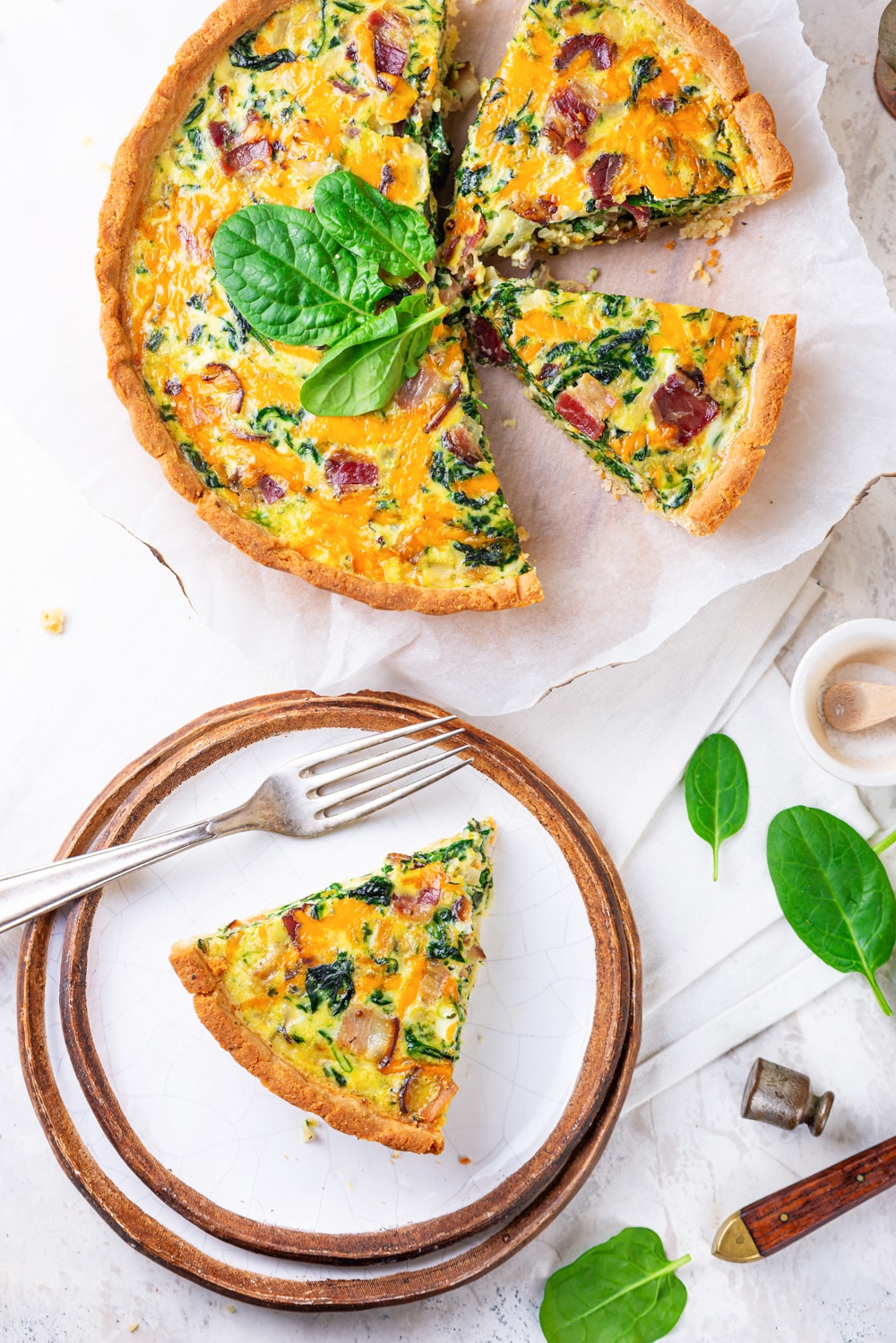 A slice of keto quiche on a plate, while the rest of the quiche is set and cut next to it.