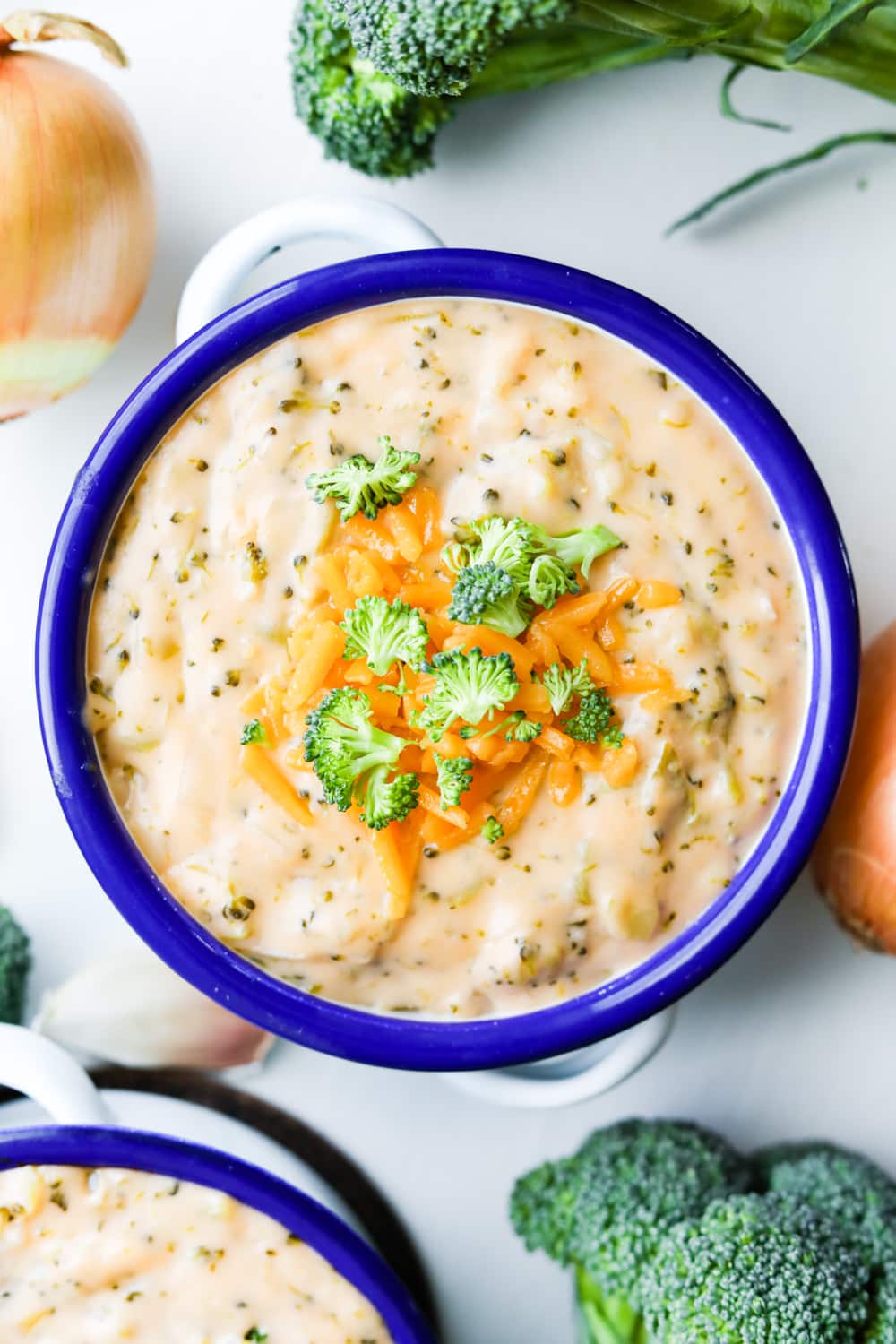 Keto broccoli cheese soup surrounded by onions and heads of broccoli.