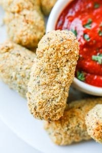 A keto mozzarella stick next to a cup of marinara sauce.