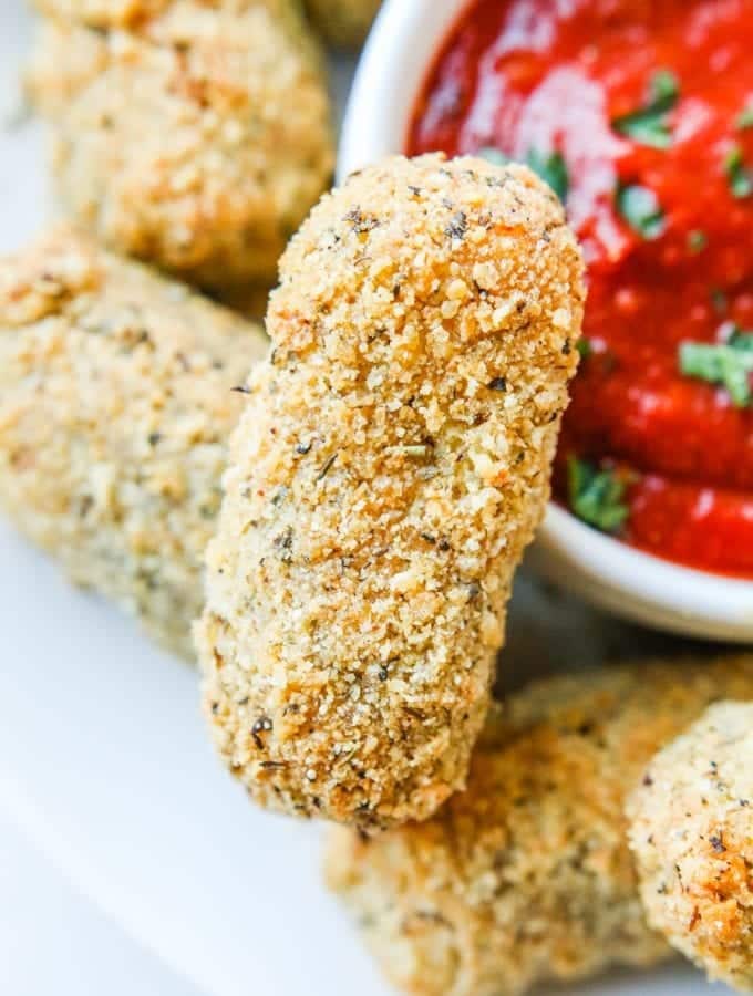 A keto mozzarella stick next to a cup of marinara sauce.