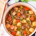 A pot with chunks of meat, carrots, and kohlrabi sitting in a broth, and topped with fresh herbs.