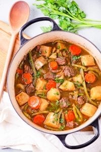 A pot with chunks of meat, carrots, and kohlrabi sitting in a broth, and topped with fresh herbs.