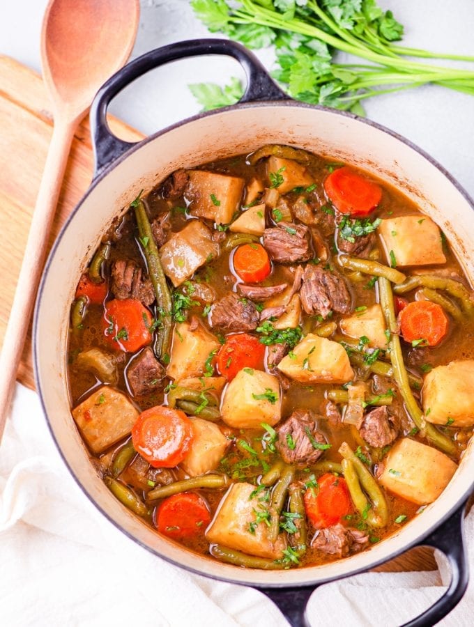 A pot with chunks of meat, carrots, and kohlrabi sitting in a broth, and topped with fresh herbs.