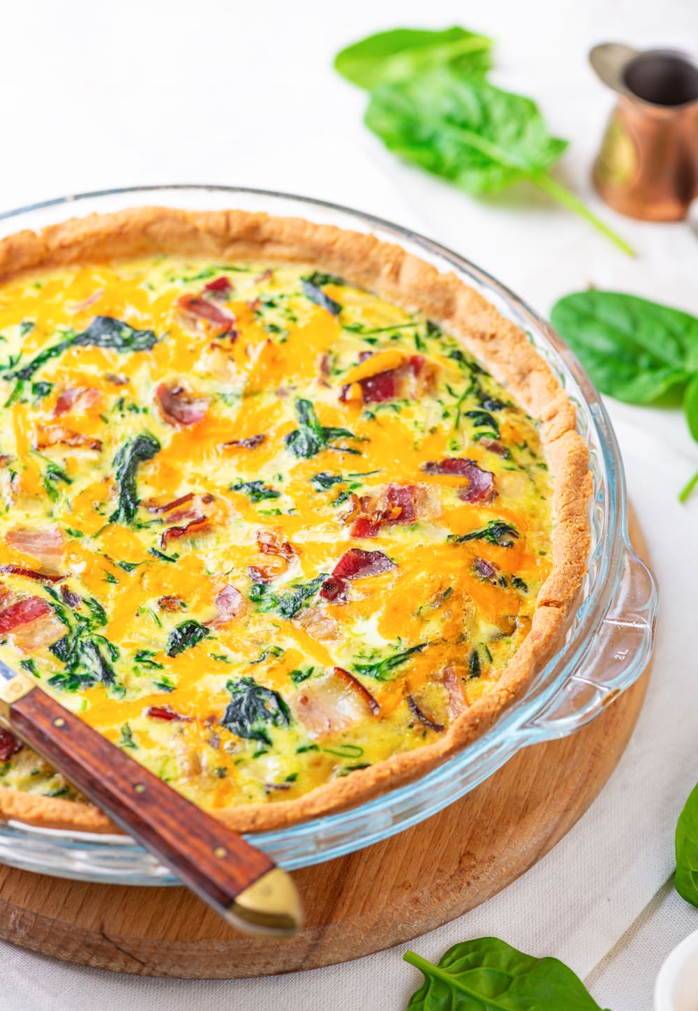 A bacon and spinach keto quiche set in a pie plate with a knife on top of it.