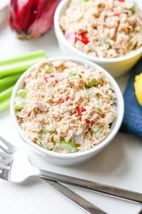 2 Bowls of tuna salad with and onion, lemon, celery, and forks next to them.