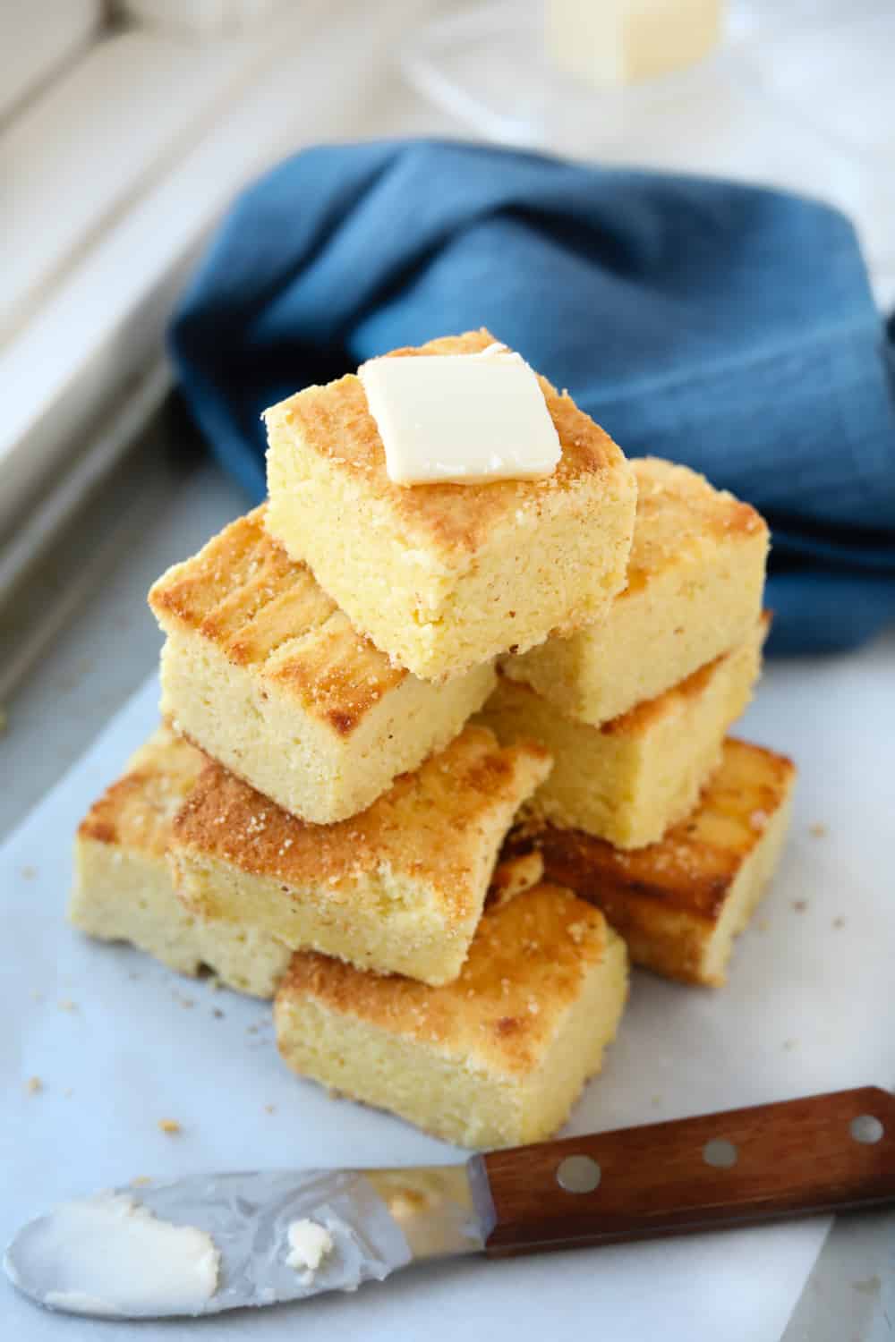 A baking sheet lined with parchment paper with slices of cornbread stacked on it.