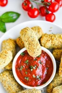 A mozzarella stick on a bowl of marinara sauce.