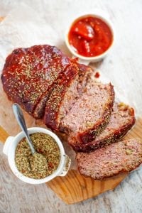 Sliced meatloaf on a cutting board with spices and ketchup next to it.