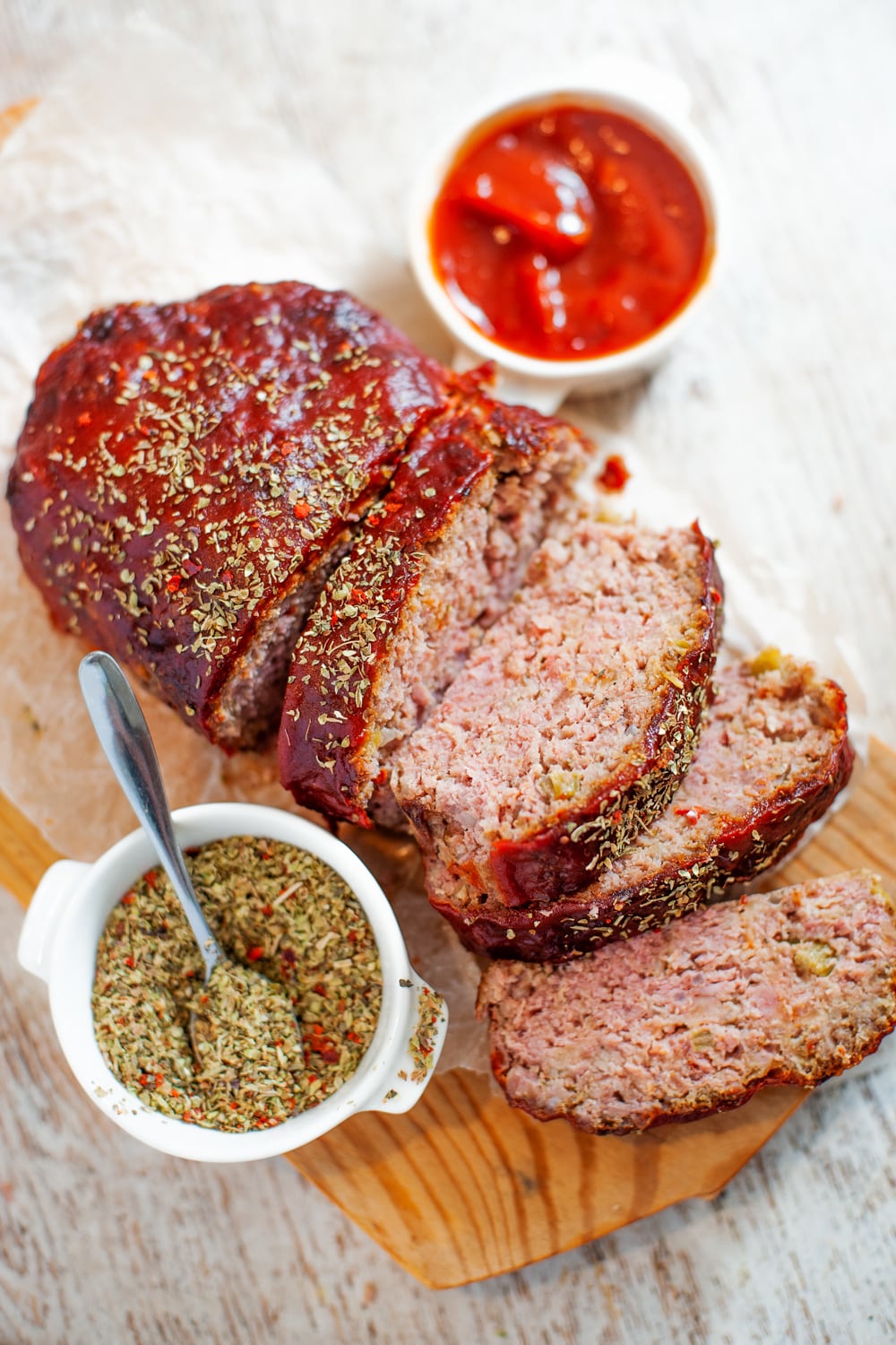 Sliced meatloaf on a cutting board with spices and ketchup next to it.