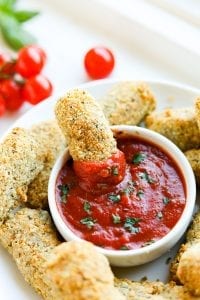 A keto mozzarella stick being dipped into a bowl of marinara sauce.