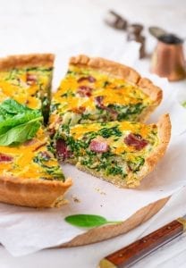 A slice of bacon and spinach quiche on parchment paper.