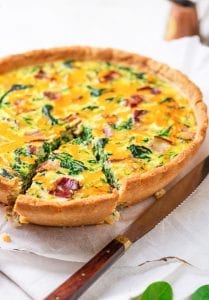 A quiche with one slice cut from it.
