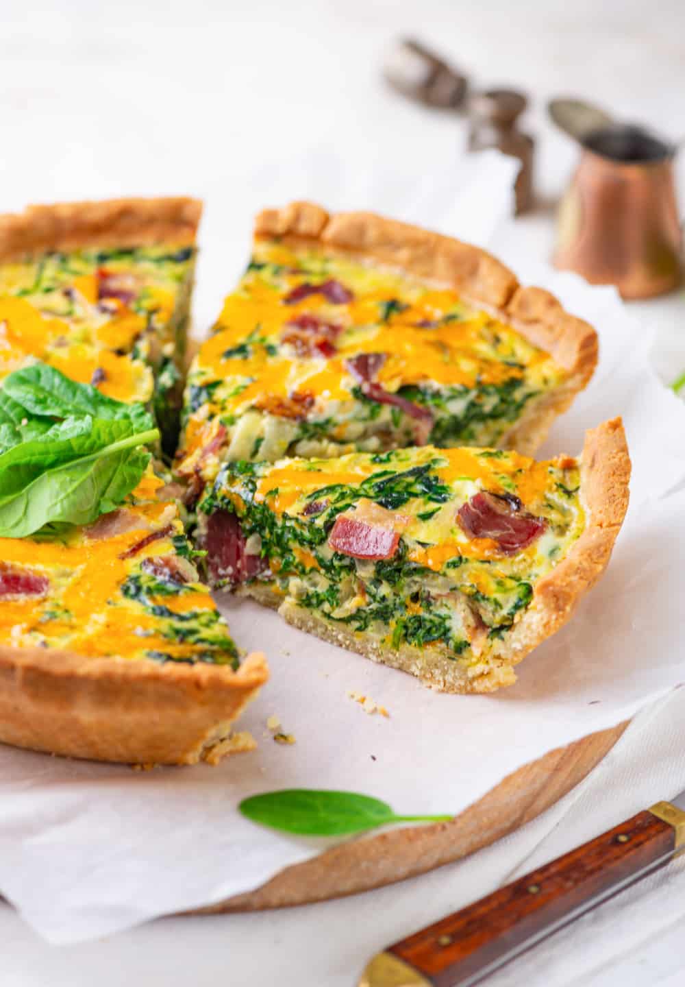 A slice of bacon and spinach quiche on parchment paper.