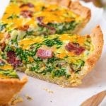 A slice of keto quiche filled with bacon and spinach set on top of parchment paper.