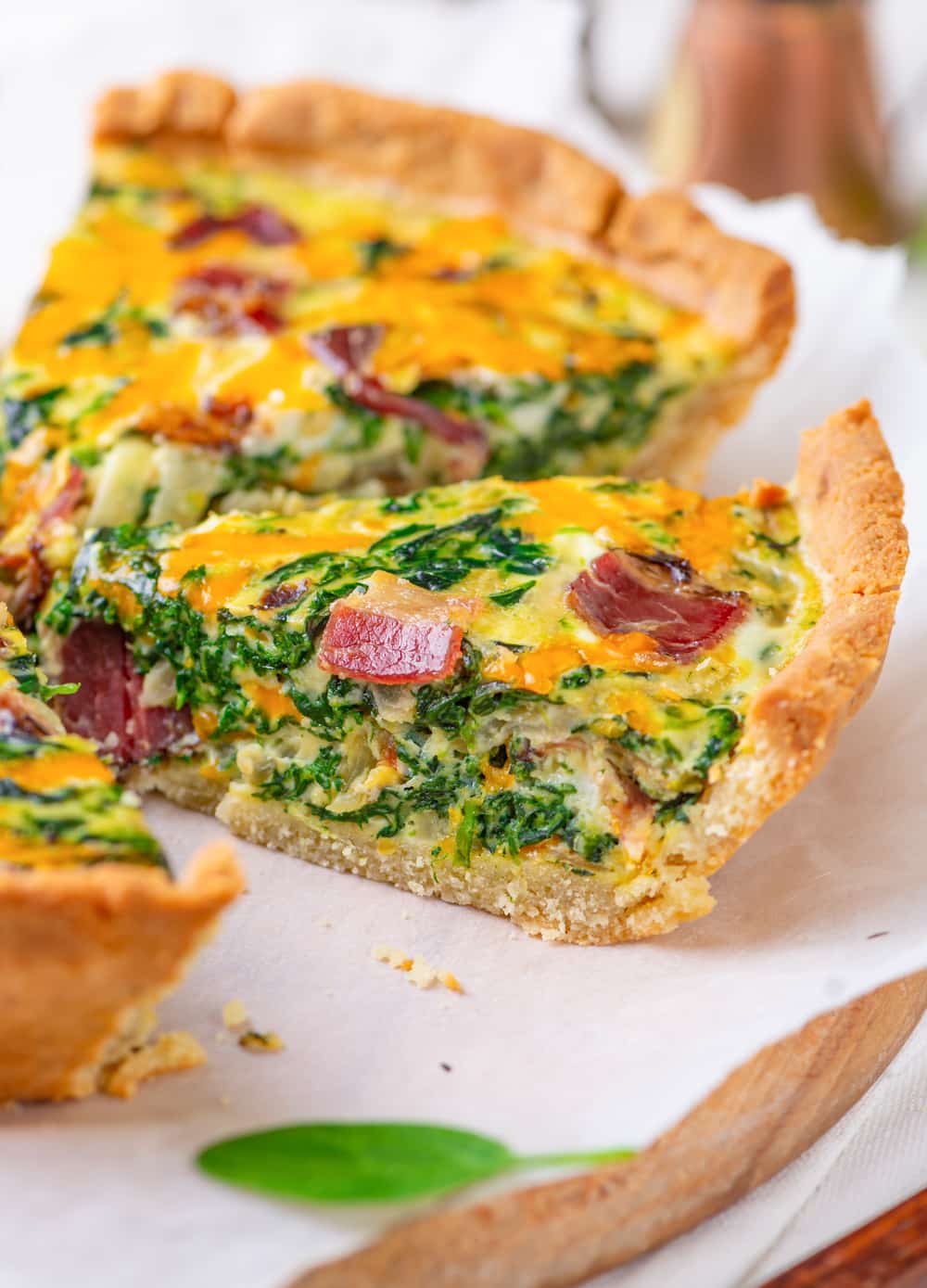 A slice of keto quiche filled with bacon and spinach set on top of parchment paper.