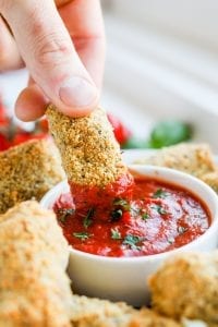 A mozzarella stick being pulled out of a cup of marinara sauce.