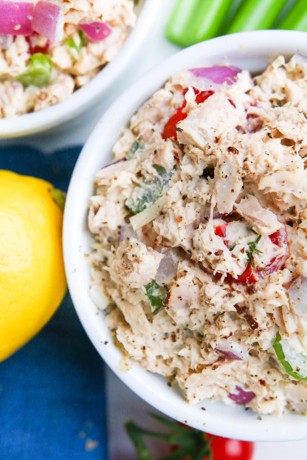 Two bowls of low carb tuna salad with a lemon, celery, and a blue napkin next to them.