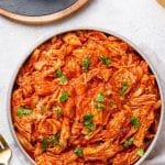 BBQ Shredded Chicken in a grey bowl topped with fresh herbs next to a grey napkin, and a fork.