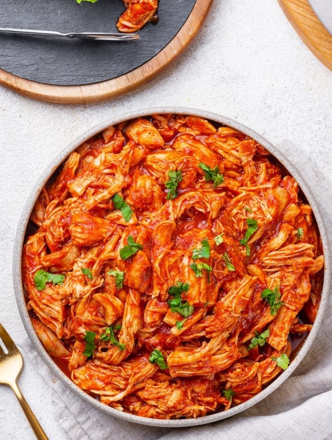 BBQ Shredded Chicken in a grey bowl topped with fresh herbs next to a grey napkin, and a fork.