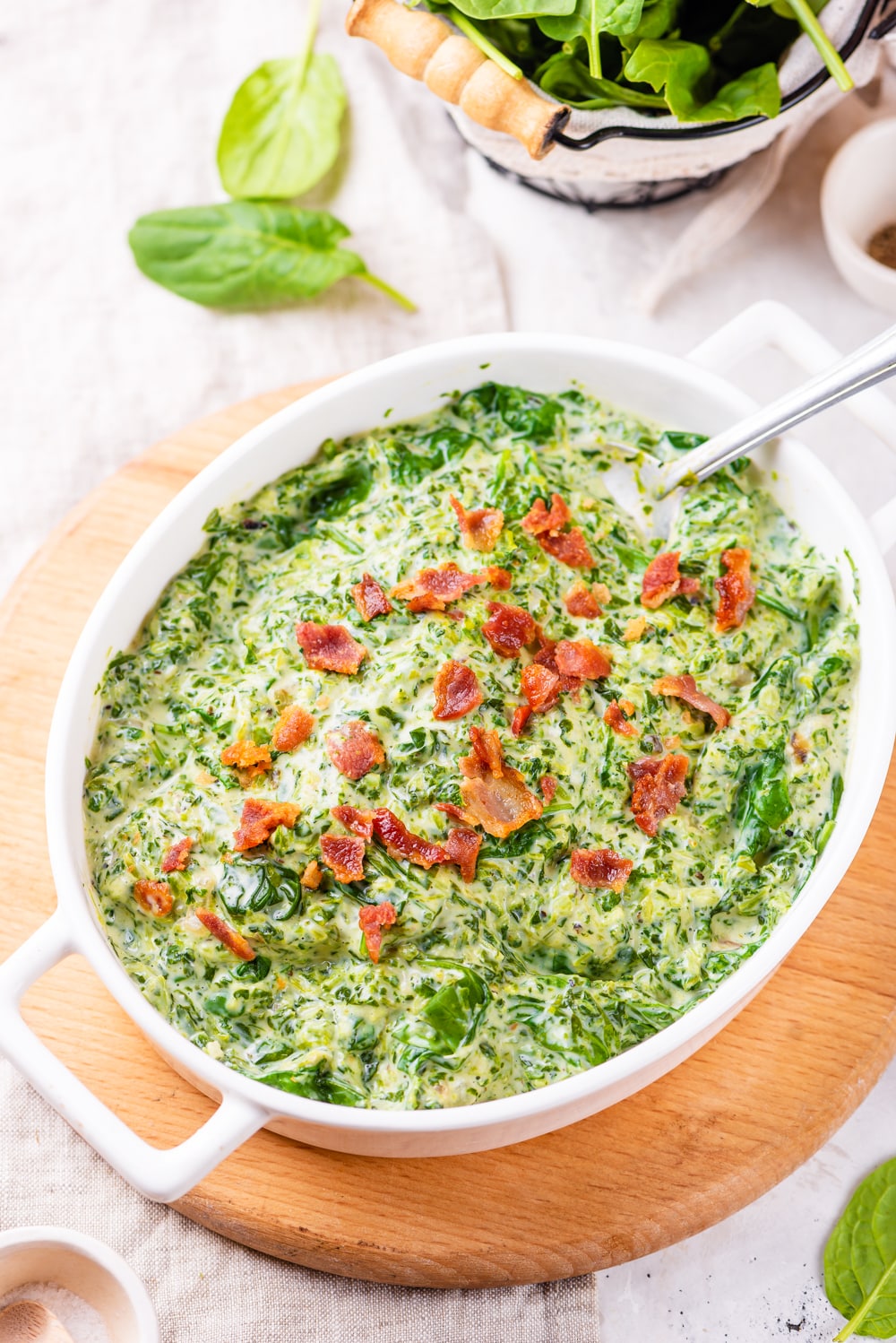 A large casserole dish filled with creamed spinach and topped with bacon.