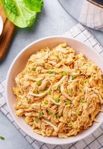 Shredded Buffalo chicken in a white bowl topped with green onions.