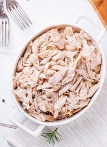 All white meat chicken shredded in a white casserole dish.