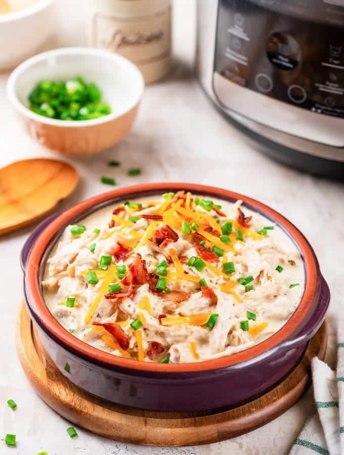 A bowl of keto crack chicken in front of an instant pot.