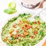 Creamed spinach in a white casserole dish topped with bacon.