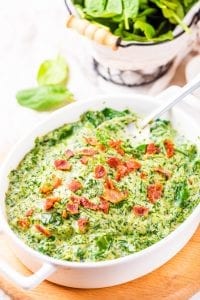Creamed spinach in a white casserole dish topped with bacon.
