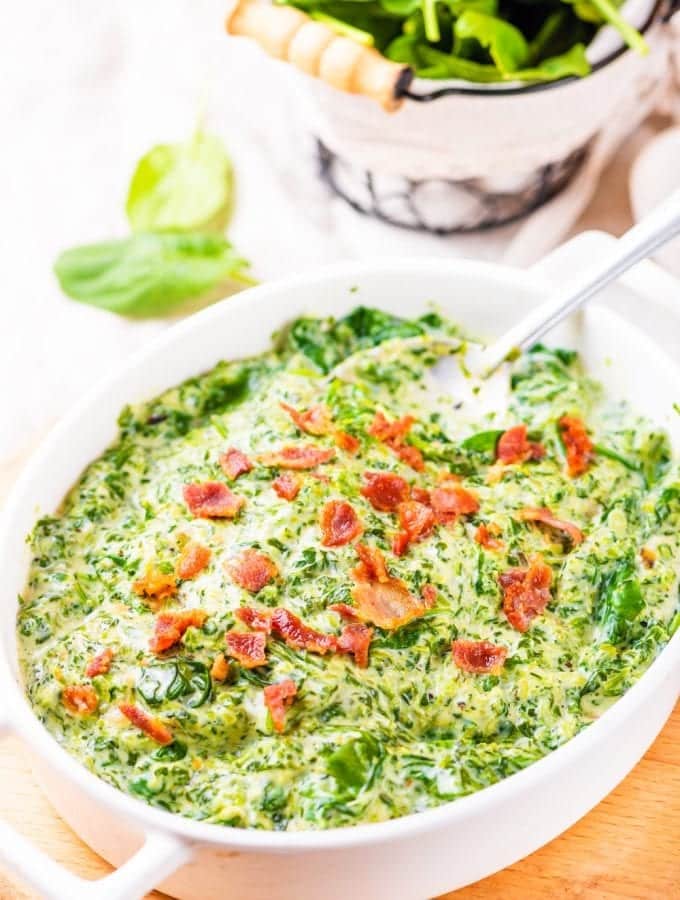 Creamed spinach in a white casserole dish topped with bacon.