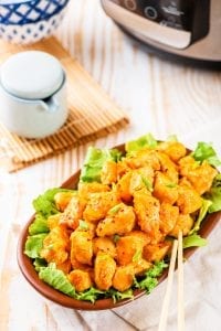 A brown bowl filled with lettuce and topped with orange chicken.