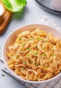 Shredded Buffalo chicken in a white bowl, and topped with green onions.