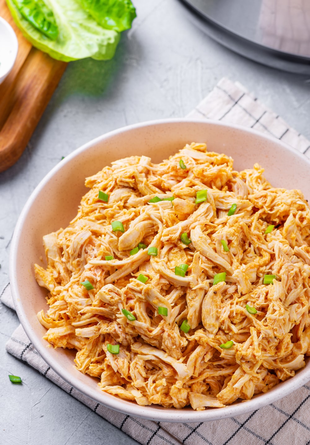 Shredded Buffalo chicken in a white bowl, and topped with green onions.