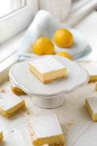 A keto lemon bar on a serving dish with lemons behind it.