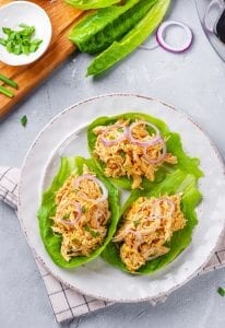 3 Buffalo chicken lettuce wraps topped with green and red onions on a white plate.