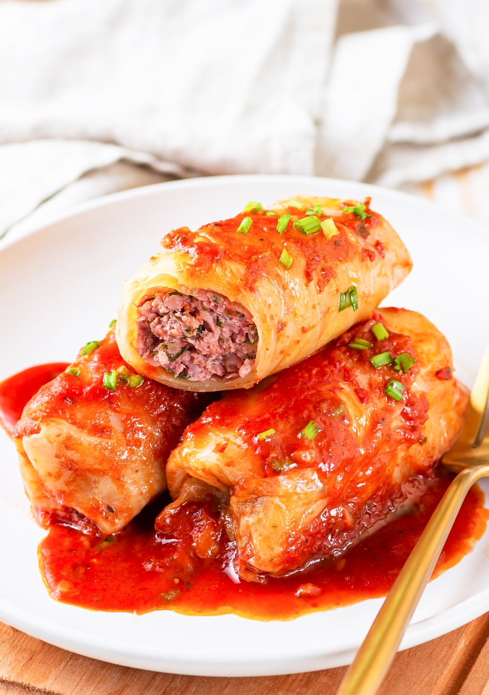 3 Cabbage rolls on a white plate with one of the cabbage rolls cut open.