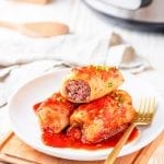 3 Cabbage rolls on a white plate next to a gold fork.