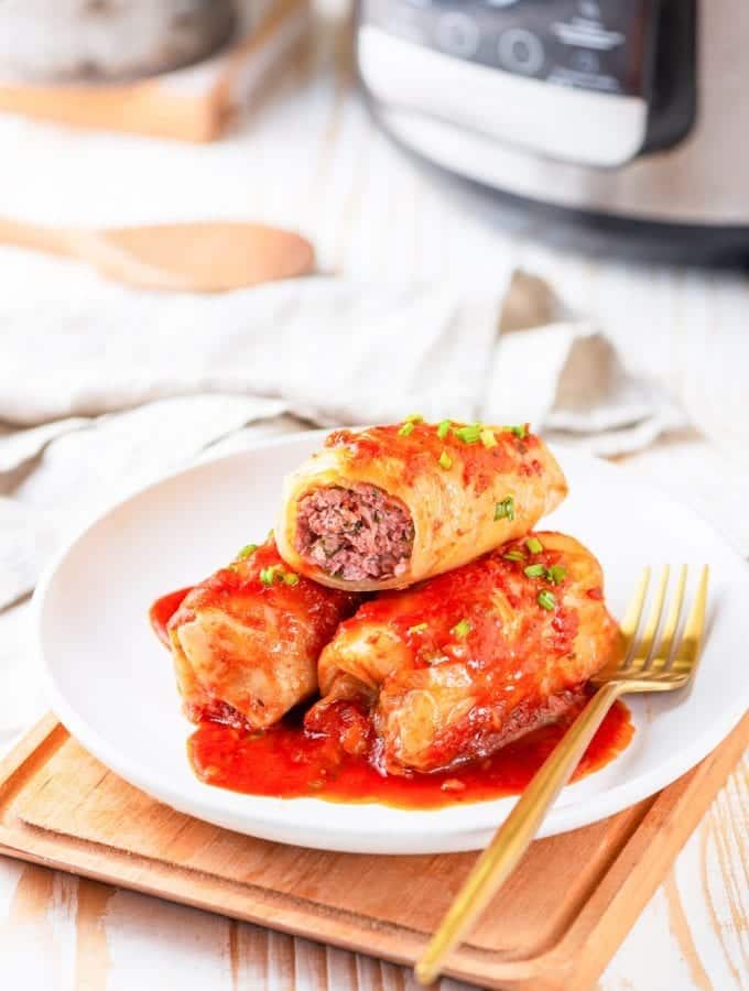 3 Cabbage rolls on a white plate next to a gold fork.