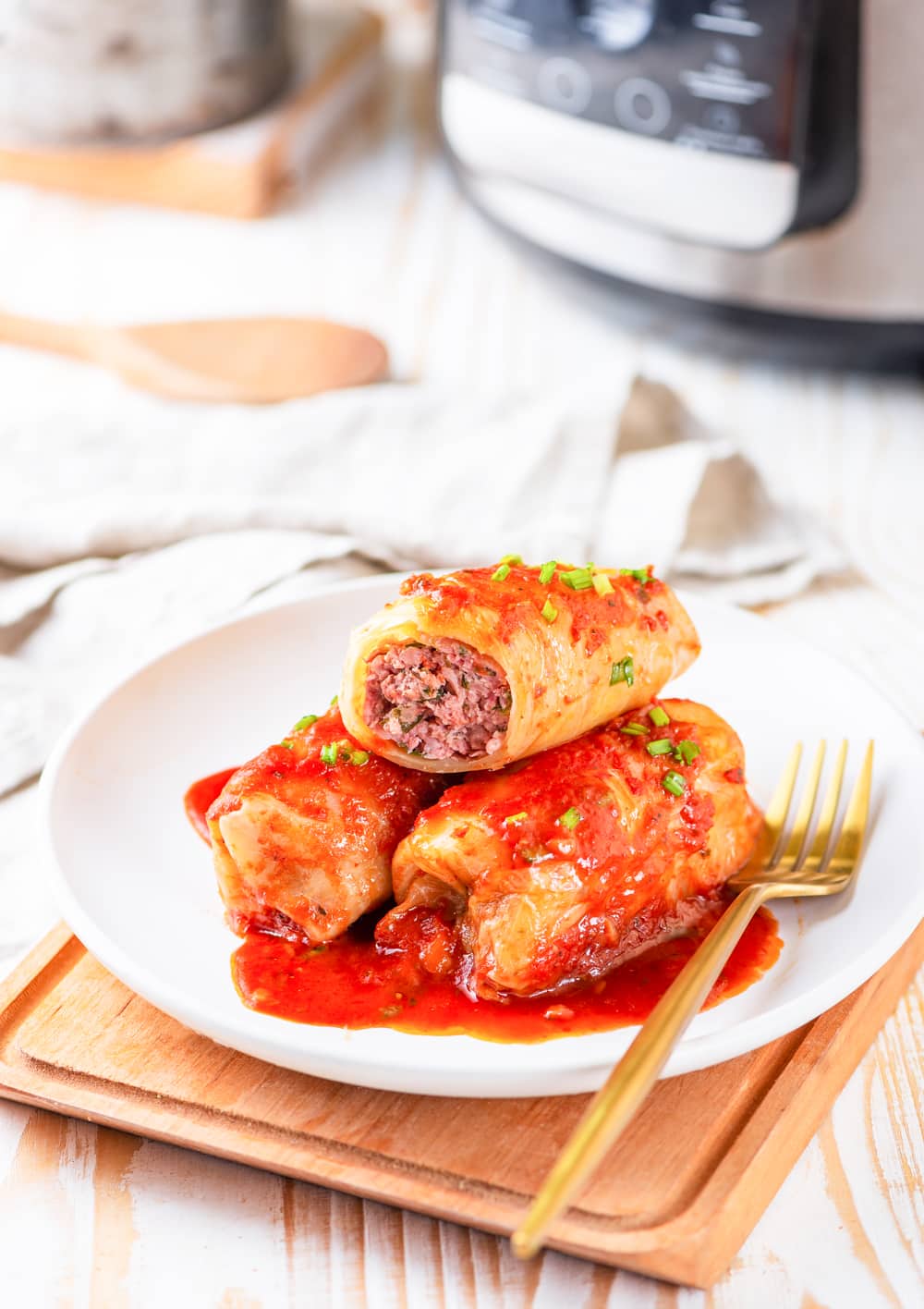 3 Cabbage rolls on a white plate next to a gold fork.