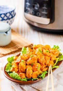 A bowl of orange chicken with an Instant Pot behind it.