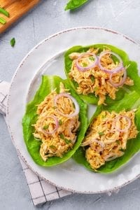 Shredded buffalo chicken placed inside 3 leafs of green lettuce, and topped with onions.